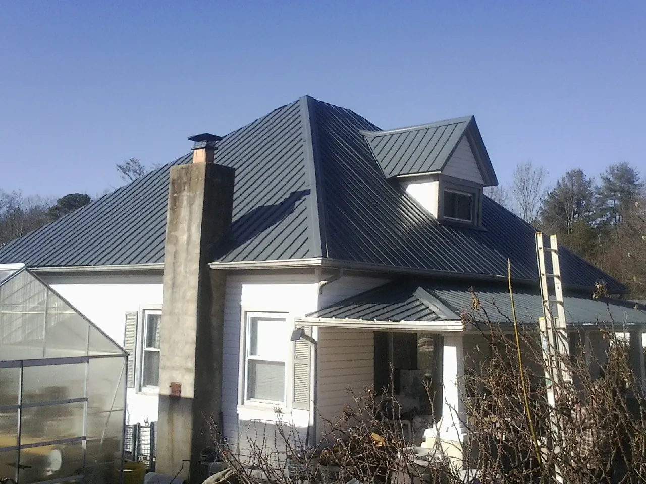 Dark blue standing seam metal roof on a white farmhouse with dormer — Slate & Tile Roof Repair by Roofing Brothers in Monclova