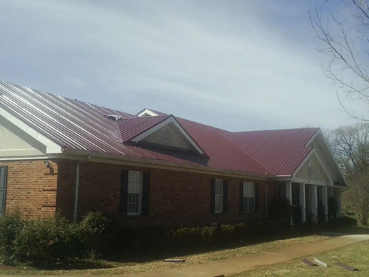 Red metal roof with gabled entries on a long brick building, from a Hail Damage Roof Repair job in Monclova