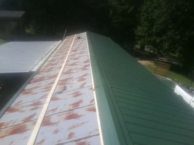 Old rusted panels beside newly installed green metal roofing — Wind Damage Roof Repair by Roofing Brothers in Monclova