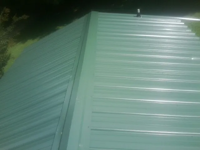 New green metal panels meeting at the ridge of a roof — Flat Roof Repair work by our crew in Monclova