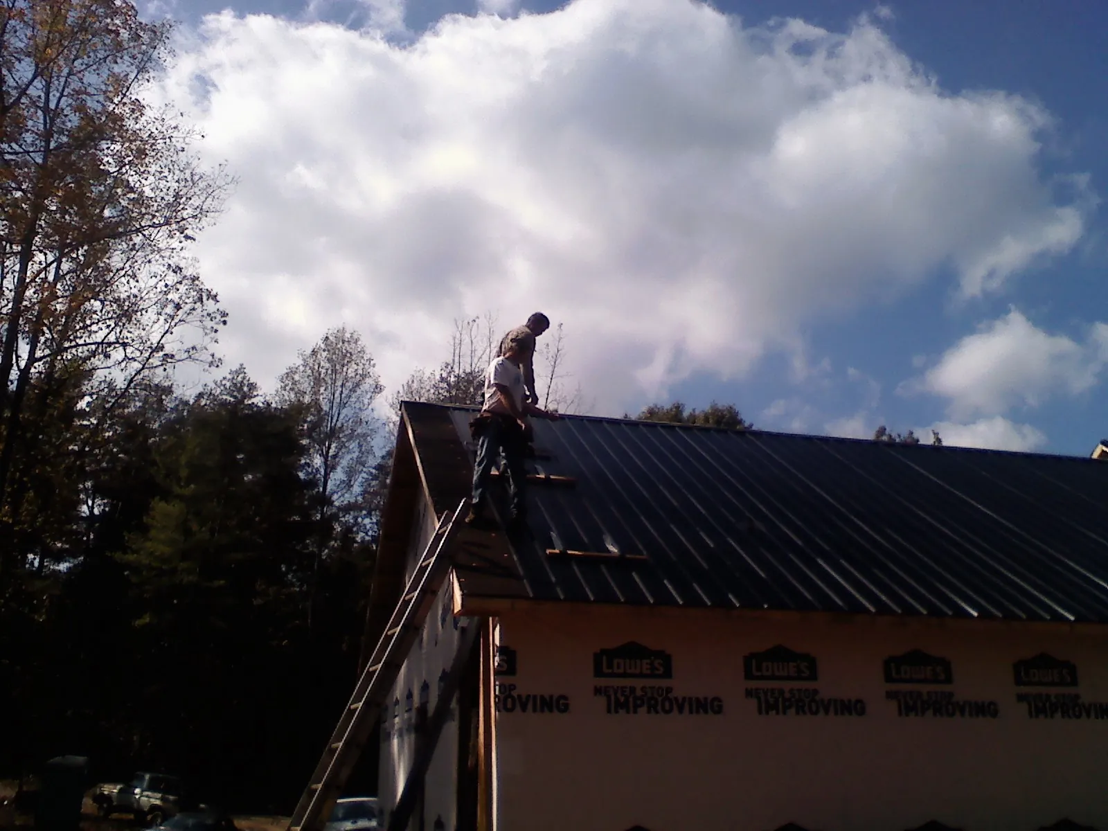 Roofer fastening dark metal panels high against a cloudy sky, from a Roof Inspection job in Monclova