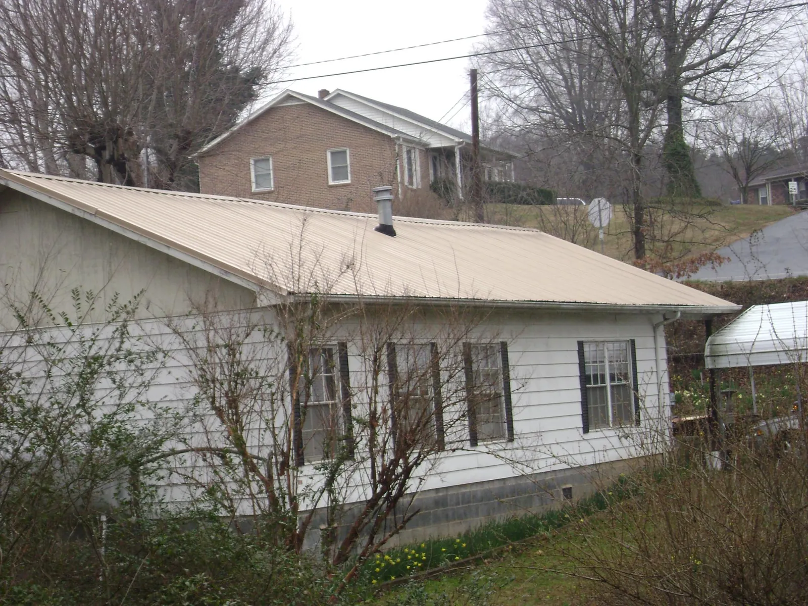 Tan metal roof on a white sided house set into a hillside — Commercial Roofing by Roofing Brothers in Monclova