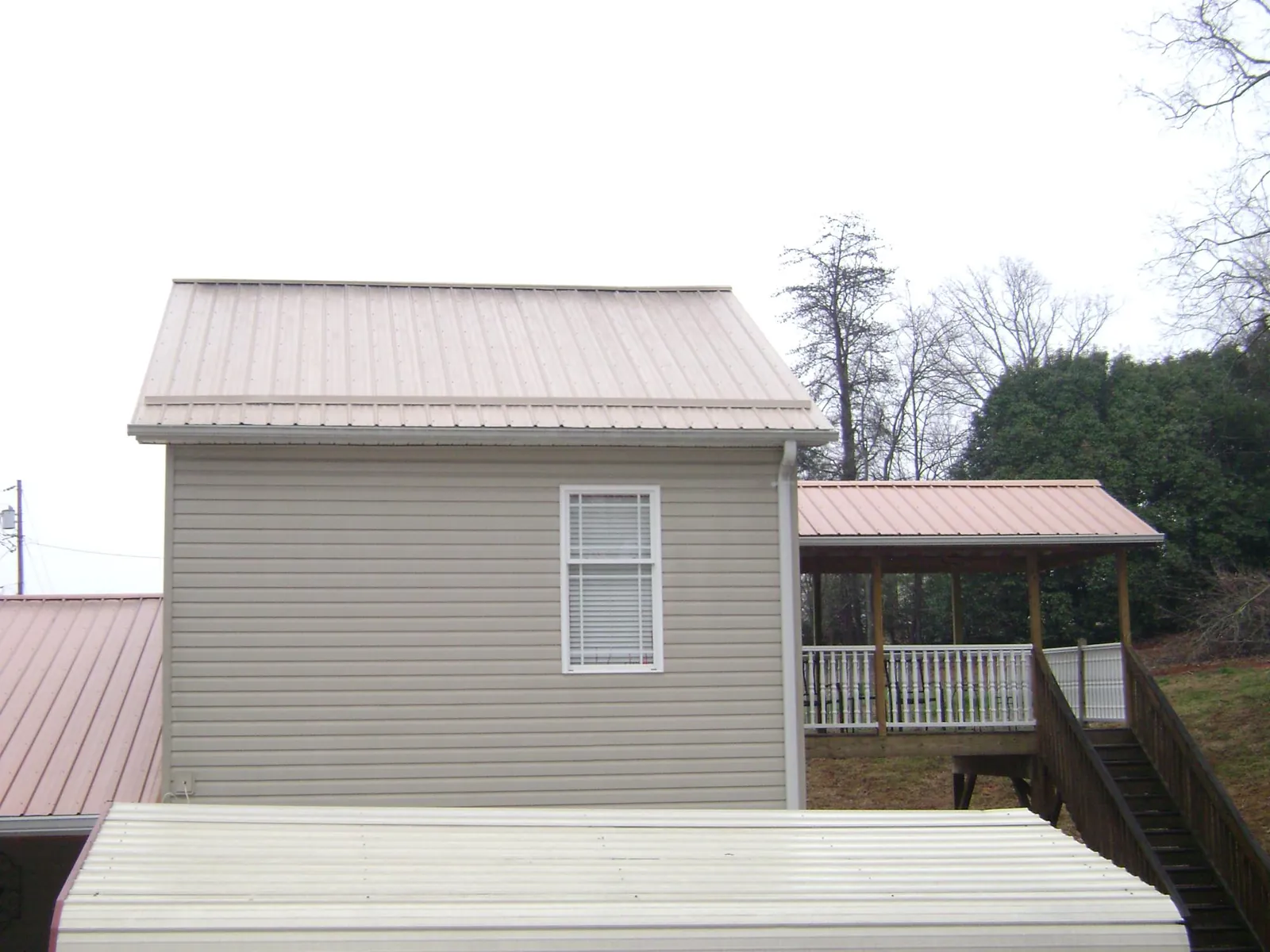 Tan metal roofs on a two story addition and attached porch, from a Roof Replacement job in Monclova